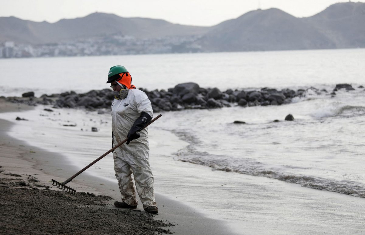 A worker cleans up an oil spill at the beach as demonstrators take part in a protest outside Repsol's La Pampilla refinery against the recent oil spill that has caused an ecological disaster on the coast of Lima, in Ventanilla, Peru January 29, 2022. REUTERS/Angela Ponce