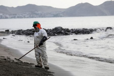 A worker cleans up an oil spill at the beach as demonstrators take part in a protest outside Repsol's La Pampilla refinery against the recent oil spill that has caused an ecological disaster on the coast of Lima, in Ventanilla, Peru January 29, 2022. REUTERS/Angela Ponce