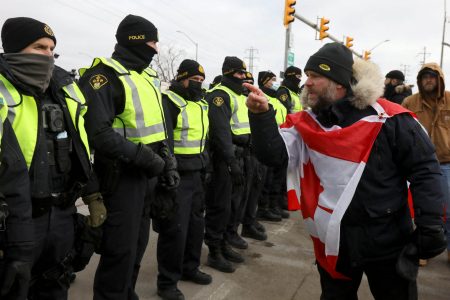 A protester gestures towards police officers, who stand guard on a street after Windsor Police said that they are starting to enforce a court order to clear truckers and supporters who have been protesting against coronavirus disease (COVID-19) vaccine mandates by blocking access to the Ambassador Bridge, which connects Detroit and Windsor, in Windsor, Ontario, Canada February 12, 2022. REUTERS/Carlos Osorio