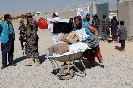 An UNHCR worker pushes a wheelbarrow loaded with aid supplies for a displaced Afghan family outside the distribution center as a Taliban fighter secures the area on the outskirts of Kabul, Afghanistan October 28, 2021. (REUTERS/Zohra Bensemra photo) 