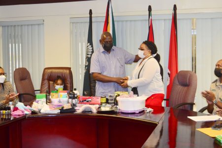 Minister of Home Affairs Robeson Benn hands over the items to Cristy Griffith yesterday in the presence of her youngest child as Permanent Secretary of the Ministry of Home Mae Thomas (seated to left) and Director of Prisons (ag) Nicklon Elliott (seated right) watch on (Orlando Charles photo)