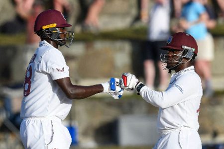 Jason Holder (left) and Nkrumah Bonner meet mid-pitch during their half-century stand on yesterday’s second day of the first Test. (Photo courtesy CWI Media)