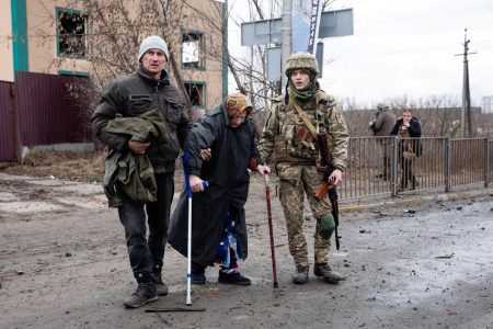 As evacuees fleeing Ukraine-Russia conflict, a Ukrainian service member assists an elderly woman walk along a road in the town of Irpin in the Kyiv region, Ukraine, on March 5, 2022. | Photo Credit: Reuters
