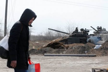 A man carries his belongings while walking along a road past tanks of pro-Russian troops during Ukraine-Russia conflict on the outskirts of the besieged southern port city of Mariupol, Ukraine, Mar 20, 2022. REUTERS/Alexander Ermochenko