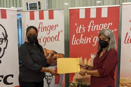Marketing Officer of KFC Guyana Ltd Pamela Manasseh (left ) delivers a cheque for $250,000 to Guyana Chess Federation Company Secretary Marcia Lee 