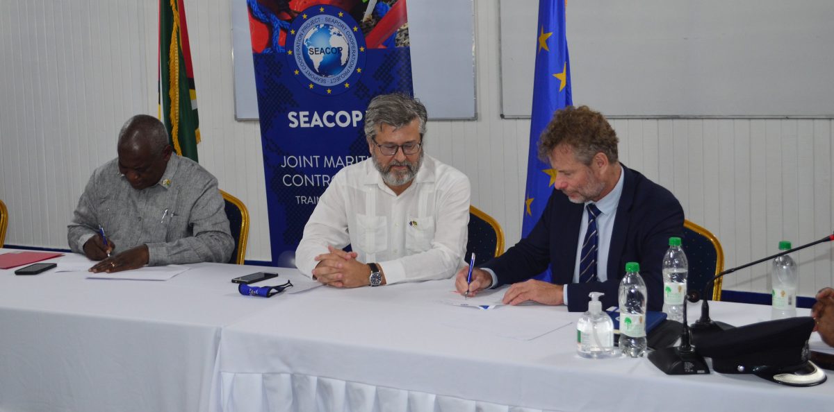 SEACOP V Project Director Dominique Bucas (at right) and Minister of Home Affairs Robeson Benn (left) sign the MOU as EU Ambassador Fernando Ponz Cantó looks on. (Orlando Charles photo)