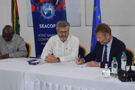 SEACOP V Project Director Dominique Bucas (at right) and Minister of Home Affairs Robeson Benn (left) sign the MOU as EU Ambassador Fernando Ponz Cantó looks on. (Orlando Charles photo)