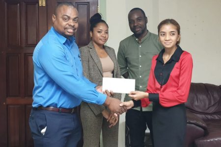 Kamari John (extreme right), representative of NHFS, hands over a cheque to organisers Jefford (extreme left) and Esan Griffith (second right) during a simple ceremony at NHFS Headquarters on Croal Street