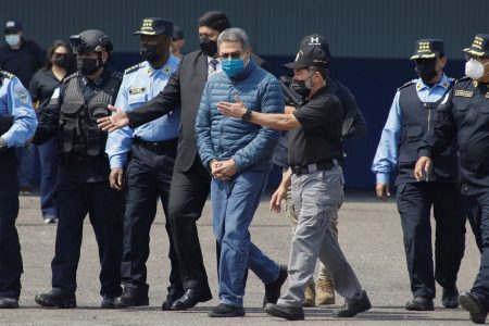 Former Honduran President Juan Orlando Hernandez, center, is taken in handcuffs to a waiting aircraft as he is extradited to the United States, at an Air Force base in Tegucigalpa, Honduras, Thursday, April 21, 2022. (AP Photo/Elmer Martinez)