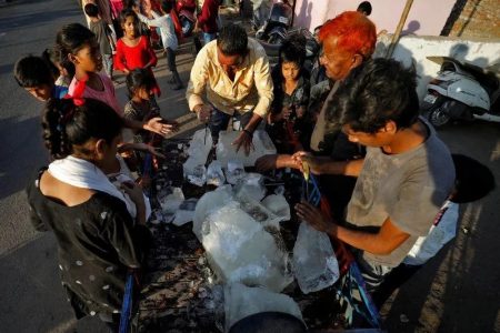 A man breaks a block of ice to distribute it among the residents of a slum during hot weather in Ahmedabad