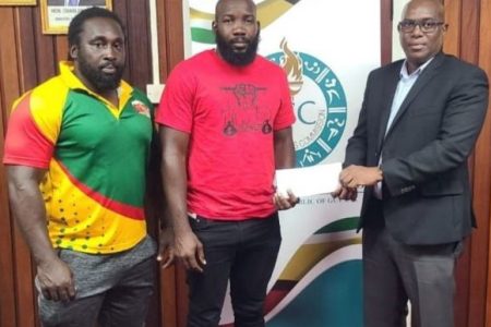 Director of Sport Steve Ninvalle presents the cheque to President of the Guyana Rugby Football Union, Ryan Dey, in the presence of Coach Theodore Henry.