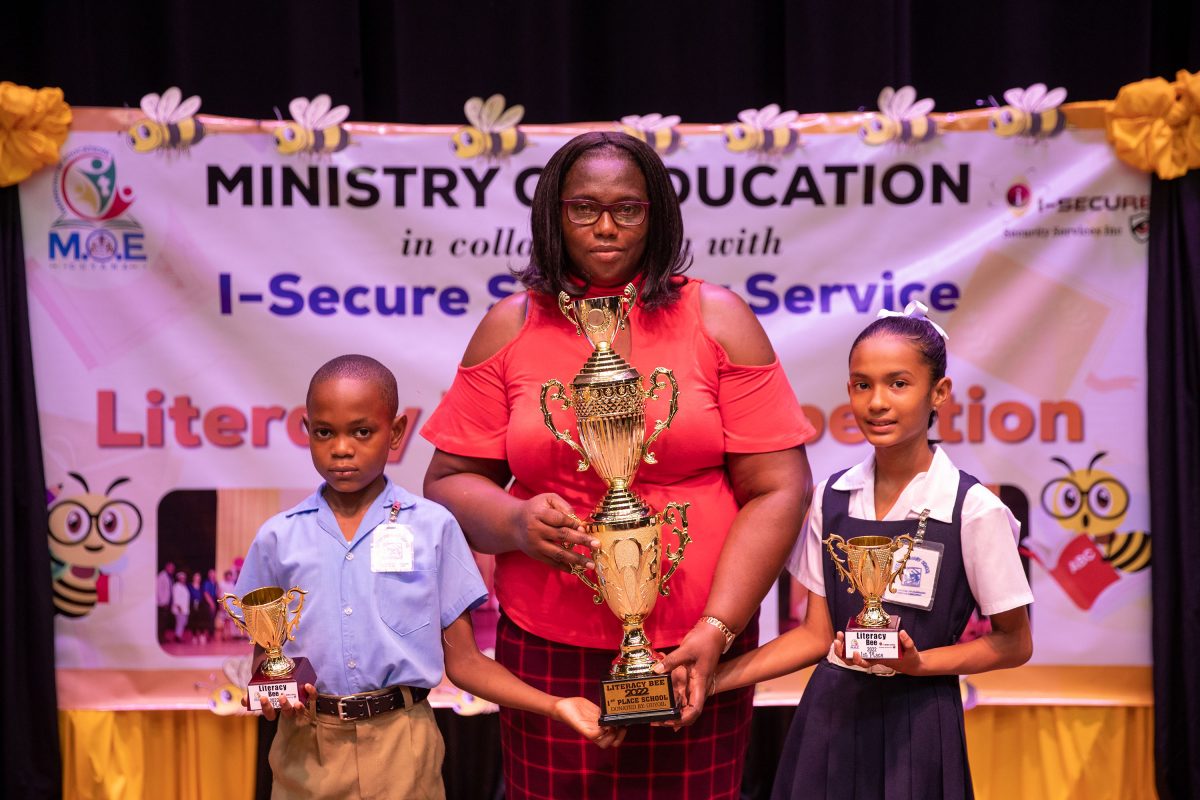 Angelina Deonarine (right) and Antwon Henry (left) of Ketley Primary School pose with their teacher after winning the 2022 National Literacy Bee. (Ministry of Education photo)