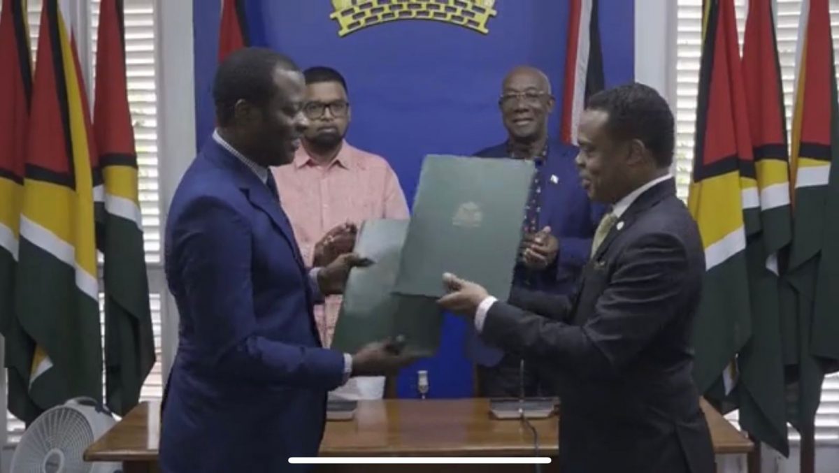 Guyana's Foreign Minister Hugh Todd (left) and Trinidad and Tobago Foreign Minister Amery Browne exchanging copies of the MoU. In the background from left are President Irfaan Ali and Prime Minister Keith Rowley.
