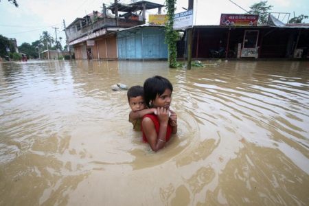 A girl carries her brother as she wades through a flooded road after heavy rains, on the outskirts of Agartala, India, June 18, 2022. REUTERS/Jayanta Dey