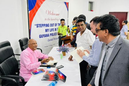 Former Commissioner of Police Seelall Persaud (seated) in conversation while autographing a copy of his new book (Photo taken from Attorney General, Anil Nandall Facebook page)
