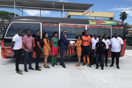 Slingerz FC President Javed Ali collecting a sponsorship cheque from DeAndrea Yansen of newest sponsor Forrester Lumberyard and Building Complex in the presence of other club officials in front of the team bus