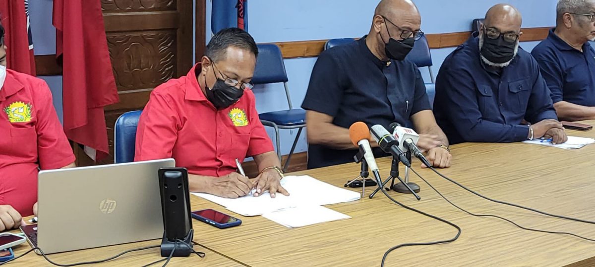 GAWU’s President Seepaul Narine (left) signs the MoC with Trinidadian OWTU President General Ancel Roget while other members look on (GAWU Photo)