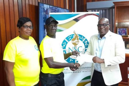 Director of Sport Steve Ninvalle hands over the first prize cheque of $300,000 to Mark Wiltshire, Organising secretary of the Georgetown Dominoes Association while assistant Organising Secretary Claire Benjamin, left, looks on.