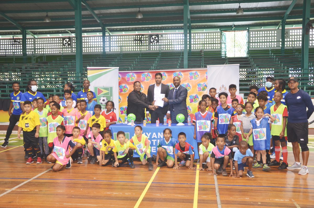 Minister of Culture, Youth and Sport Charles Ramson Jr (centre) standing alongside GFF President Wayne Forde (right), and General Manager of GBI Samuel Arjoon in the presence of children who will feature in the Kool Kidz Futsal camp.