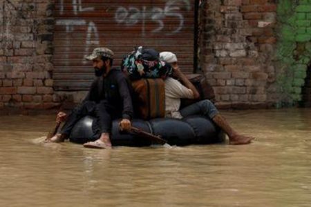 A volunteer paddles an inflatable tube as he evacuates a flood victim with his belongings, following rains and floods during the monsoon season in Charsadda, Pakistan August 27, 2022. REUTERS/Fayaz Aziz
