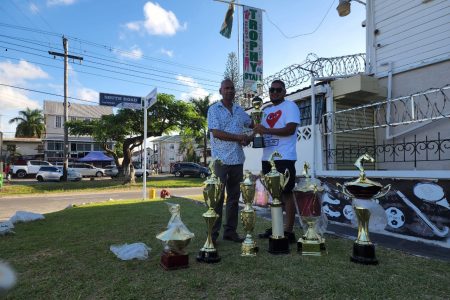 Ramesh Sunich (left), proprietor of Trophy Stall, hands over the champion jockey trophy in honour of his father, Neville Sunich, who was also a jockey, to Justin Ally, representative of the Jumbo Jet Thoroughbred racing committee. The accolade will be awarded today following the conclusion of the Guyana Cup at the Rising Sun Sports Club, West Coast Berbice.