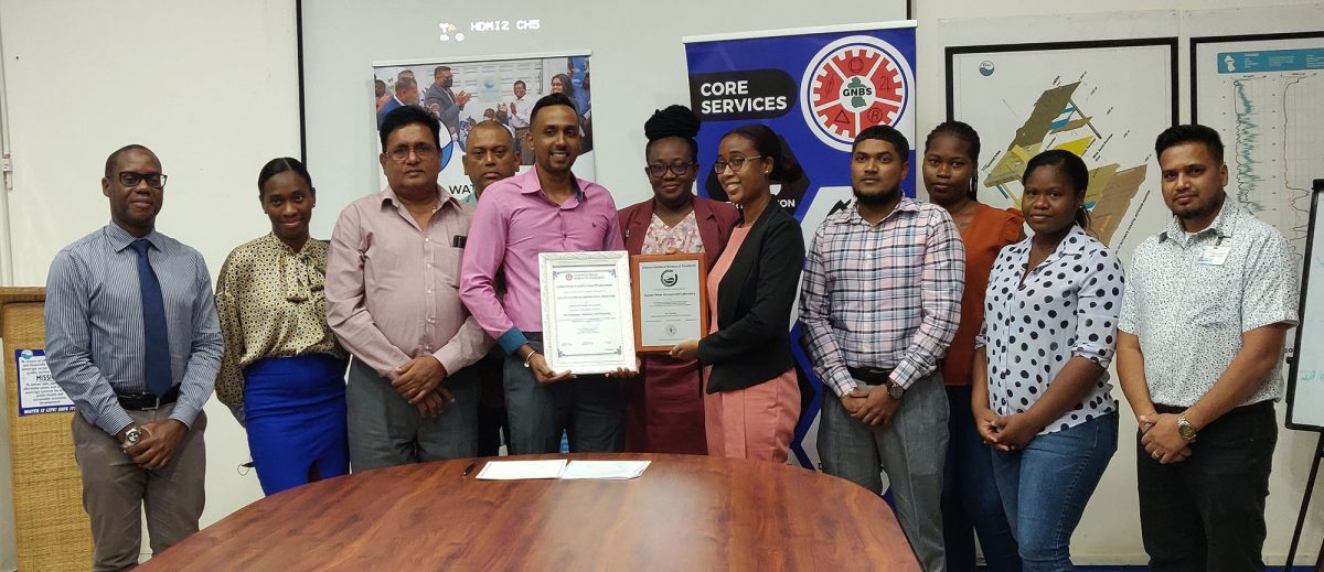 GWI’s Head of Water Quality (ag)  Avinash Parsram (left of centre) and Laboratory Quality Officer,  Angela Fordyce, surrounded by GWI & GNBS staff, display the certificate & plaque presented to them by GNBS. (GWI photo)
