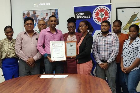 GWI’s Head of Water Quality (ag)  Avinash Parsram (left of centre) and Laboratory Quality Officer,  Angela Fordyce, surrounded by GWI & GNBS staff, display the certificate & plaque presented to them by GNBS. (GWI photo)

