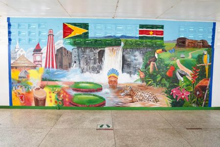 The Guyana Tourism Authority (GTA) on Tuesday unveiled a tourism mural at the Canawaima Ferry Terminal at Moleson Creek, Berbice, Region Six, as part of activities organised to mark World Tourism Day. According to the Department of Public Information, the artist, Colin Nedd, stated that the painting represents tourism in Guyana as it depicts culture, heritage, flora, fauna, and wildlife. “I’m glad to represent the Ministry of Tourism at this level. I did a lot of other works that people may recognise in Guyana like, for instance, the paintings in the zoo,” said Nedd, who described his artistic style as a mixture of realism and symbolism. Kaieteur Falls, the Umana Yana, St George’s Cathedral, the National Flags of Guyana and Suriname, and the Victoria Regia Lily are some of the elements of the mural, which is Nedd has painted. (Department of Public Information photo)
