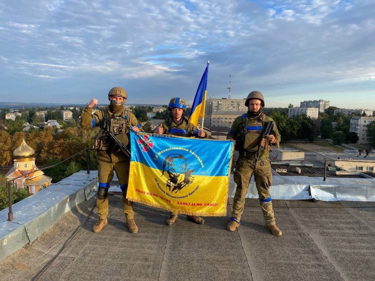 Ukrainian soldiers pose with a flag after retaking the town of Kupiansk near Kharkiv from Russian force, September 10, 2022.