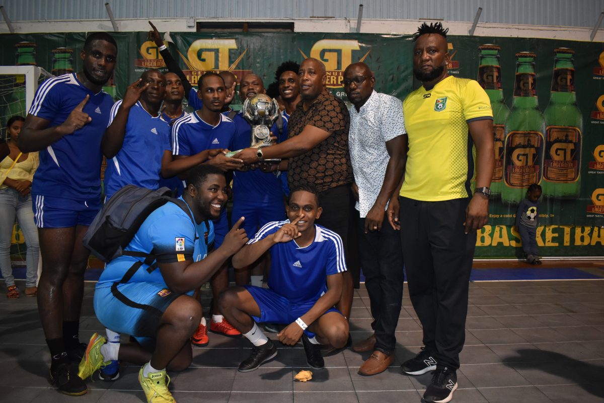 Gregory Richardson of Sparta Boss receives the championship trophy and first place prize from Banks DIH Ltd. Outdoor Events Manager Mortimer Stewart in the presence of teammates and other tournament officials