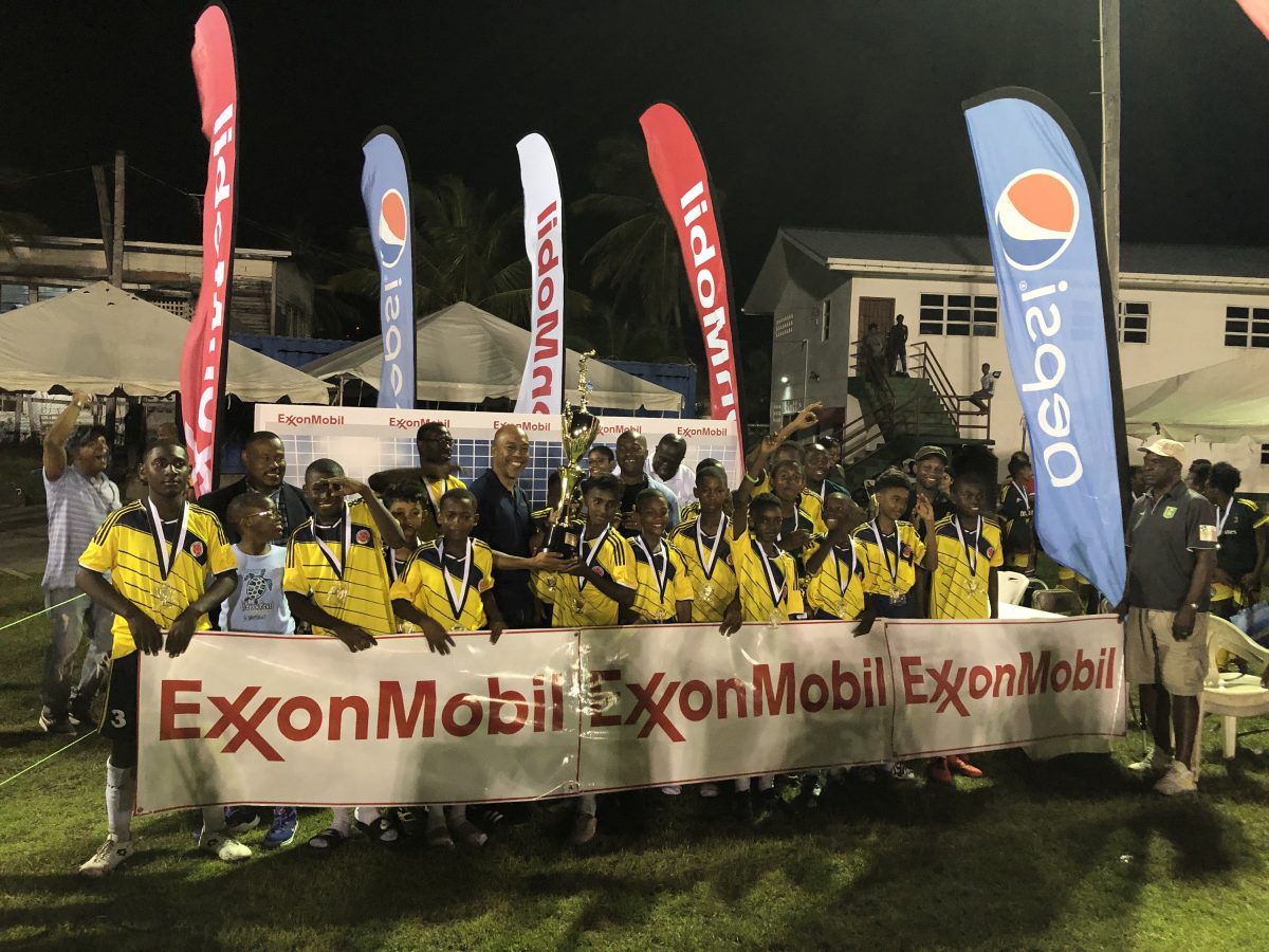 Marcus Tripp, Senior Director of Government and Public Affairs of ExxonMobil, presents the championship trophy to Charlestown captain Malcolm Hendricks in the presence of teammates, sponsors, and tournament officials