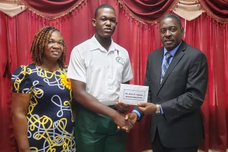 Pastor Exton Clarke, President of the Guyana Conference of Seventh-day Adventists, presents the monetary award to Daniel Dowding on behalf of Dr Kurt Clarke in the presence of his mother, Sarah Dowding
