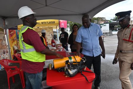  Minister of Home Affairs Robeson Benn examining safety gear, which was among the exhibits on display at the Guyana Fire Service’s Fire Safety Fair and Exhibition held at the National Park on Friday (Ministry of Affairs photo) 