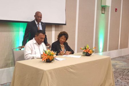 G-Invest Head Peter Ramsaroop (left) and JAMPRO President Diane Edwards signing the MOU while Jamaican Minister of Industry, Investment and Commerce, Aubyn Hill looks on.