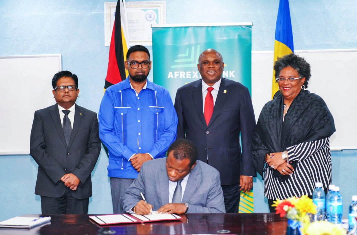 Guyana’s Minister of Foreign Affairs Hugh Todd signing the pact under the watchful eyes (from right) of Barbadian Prime Minister Mia Mottley;  President of the bank, Professor Benedict Oramah; President Irfaan Ali and Minister of Finance Dr Ashni Singh. (Office of the President photo)