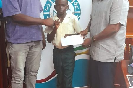 President of the Guyana Boxing Association, Steve Ninvalle (right) handing  over assistance to Keyon Britton on behalf of USA based Guyanese, Samuel Gittens. Pictured also is Technical Director of the GBA, Terrence Poole.