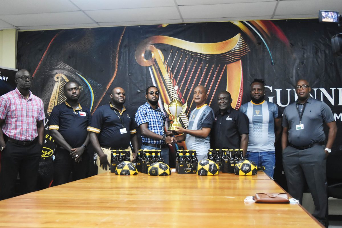 Tournament coordinator Rawle Welch (3rd from right) collecting the championship trophy from Guinness Brand Manager Jeoff Clement (3rd from left) at the official launch, while (from left) Guinness Brand Executive, Lee Baptiste; Banks DIH Ltd Supervisors, Joel Ward, and Kenneth Hazel; Banks DIH Ltd Communications Officer, Troy Peters; Referees Coordinator, Wayne Griffith; and Outdoor Events Manager, Mortimer Stewart look on
