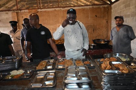 Minister of Home Affairs, Robeson Benn (centre) sampling prison food during a tour of the Mazaruni Prison on Sunday. (Ministry of Home Affairs photo)
