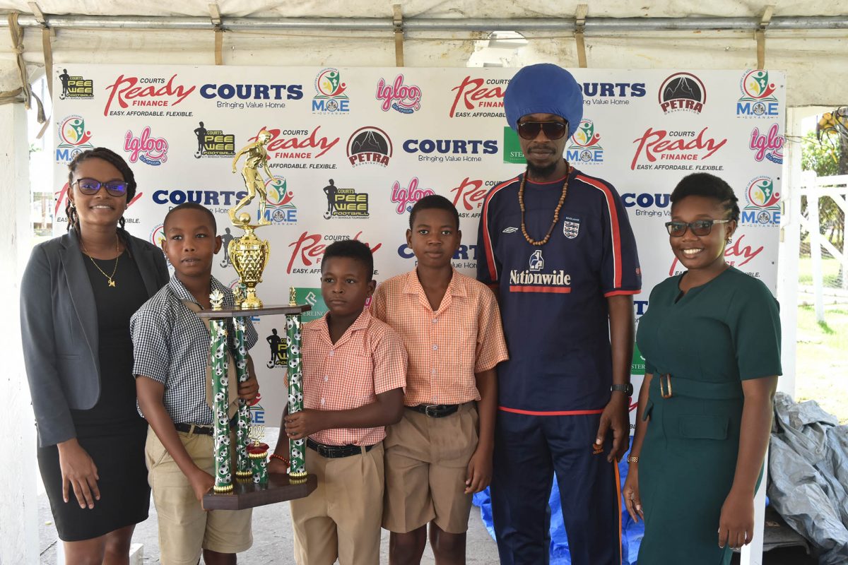 St Pius captain Omar Moses (2nd from left) and Enterprise skipper Fabio Kowlessar (3rd from left) squaring off with the championship trophy ahead of the Courts Pee Wee Boy’s U11 Football Championship match in the presence of several school officials including St Pius Manager, Melissa Rodrigues (1st from left), Enterprise forward Jayshan Haynes
(4th from left), and Enterprise head coach Troy Wright
