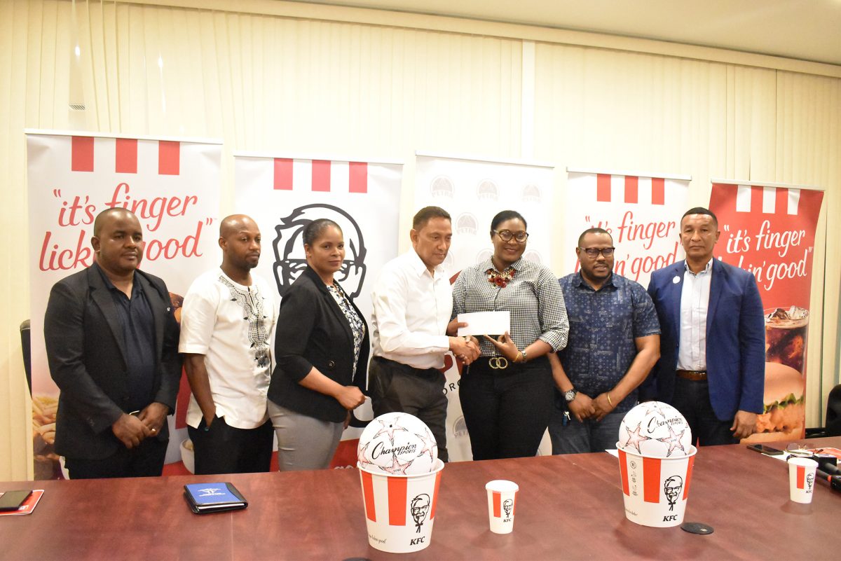 Roger Hay, Chief Executive Officer of KFC, presenting the sponsorship cheque to Petra Organization senior member Jacklyn Boodie. Also in this picture (from left to right) are: GFF Communications Director Keeran Williams, Kirk Braithwaite, Administrator of the Allied Arts Department of the Ministry of Education, Pamela Manasseh, Marketing Manager of KFC, Troy Mendonca, Co-Director of the Petra Organization, and Chairman of the National Sports Commission, Kashif Muhammad 
