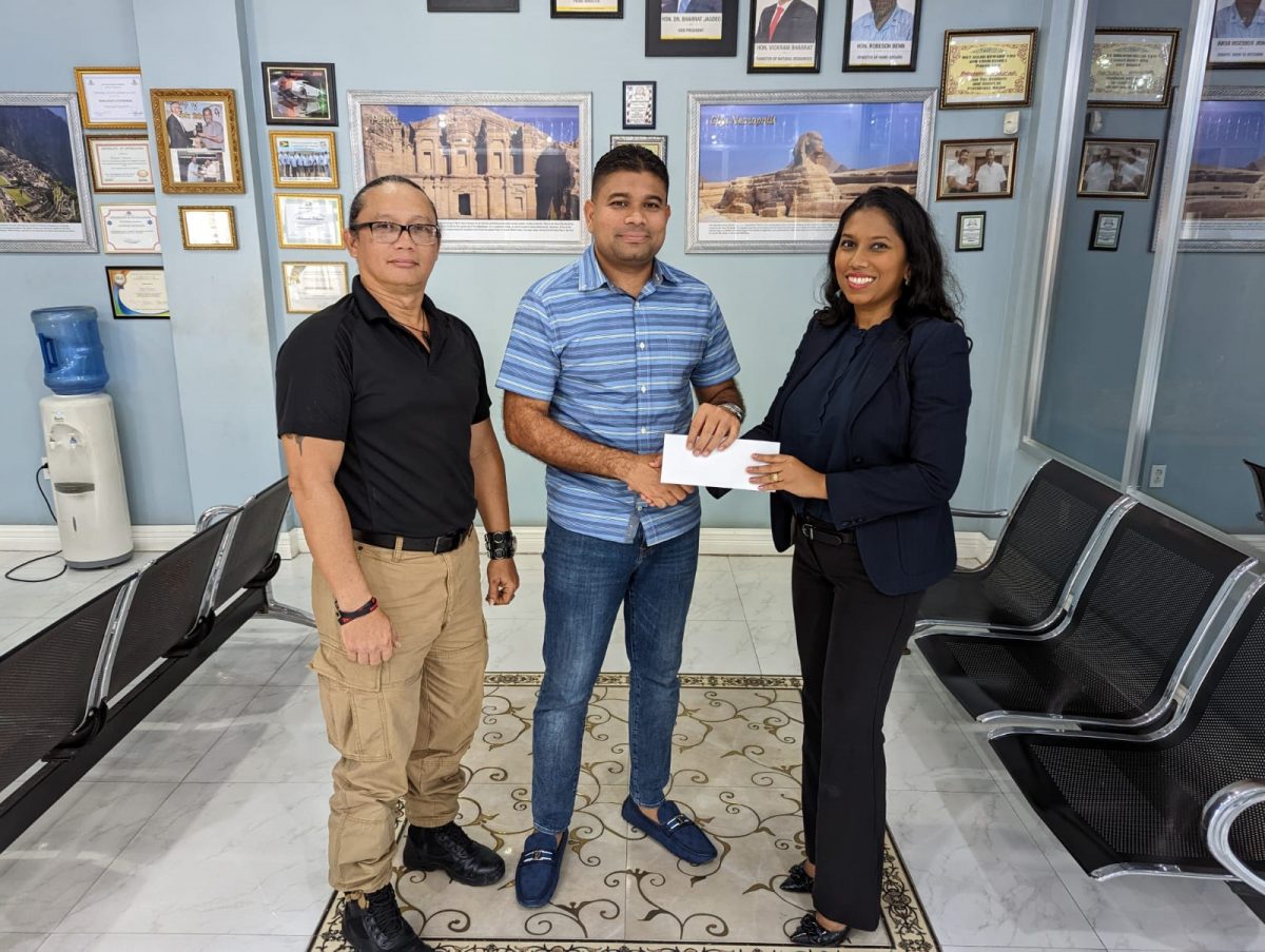 Azruddin Mohamed of Team Mohamed (centre) hands over the sponsorship cheque to Vidushi Persaud-McKinnon, Secretary-General of Archery Guyana (right) in the presence of Nicholas Hing, Head-Coach of Archery Guyana.