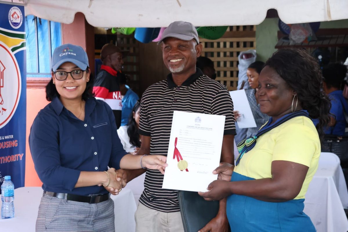 Minister within the Ministry of Housing and Water Susan Rodrigues (left) hands over a title to one of the families (CHPA/Anil Seelall photo)