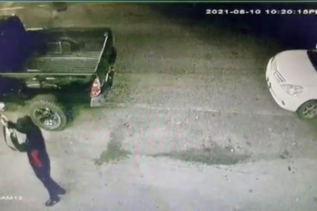 A screenshot from one of the surveillance videos showing one of the suspects (at lower left) firing at one side of the pick-up, with the getaway car parked at right.