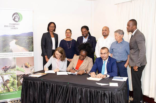 From left Dr. Antje Müllner and Permanent Secretary within the Office of the President, Abeena Moore signing the MoU in the presence of Foreign Secretary Robert Persaud, and other PAC staff (Department of Public Information photo)
