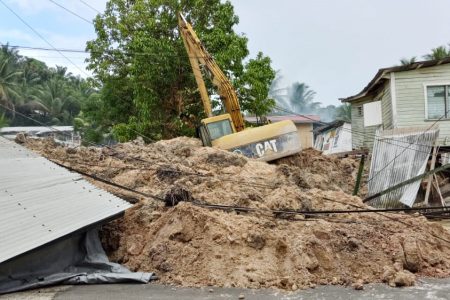 The excavator that came down with the debris. At right is one of the affected homes (Photo courtesy of Deron Adams)