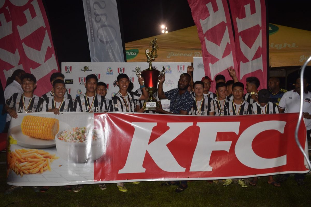 Raydon Krammer, captain of DC Caesar Fox, receives the championship trophy from KFC Home Delivery Manager Esaun Daniels in the presence of teammates following their hard-fought win over St. Benedict’s College in the final.