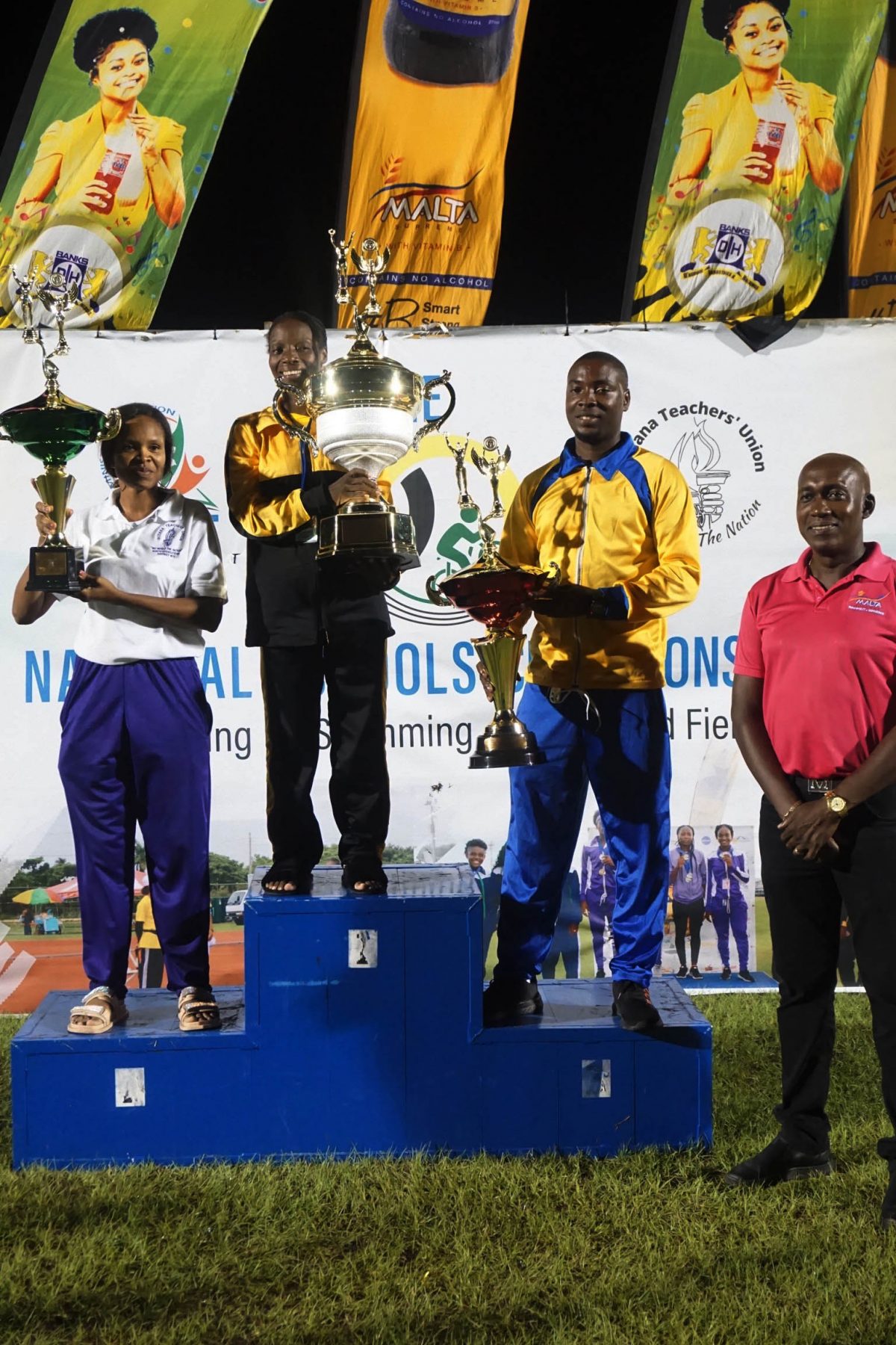Champs Again!  Representatives of District’s 11 and 3 flank the representative of District 10 who received the coveted Champion of Champions trophy during the closing ceremony of the 60th edition of the National Schools Swimming, Cycling and Track and Field Championships last night. (Emmerson Campbell photo)


