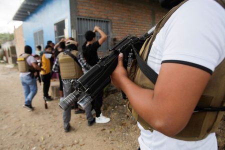 A member of Honduras' DIPAMPCO (Police Anti Maras and Gangs Against Organised Crime Directorate) stands guard as other DIPAMPCO members frisk people while doing rounds in a low-income neighbourhood, after President Xiomara Castro declared a national security emergency implementing a new plan to combat a rising number of cases of extortion by violent criminal groups operating across the country, in Tegucigalpa, Honduras November 26, 2022. REUTERS/Fredy Rodriguez/File Photo
