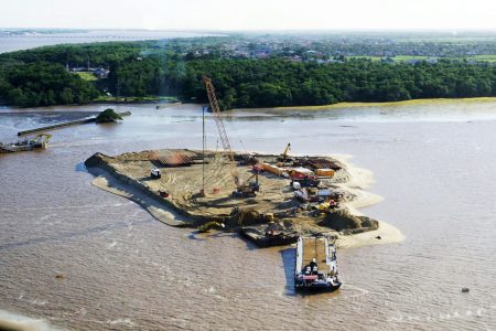  The construction of Guyana’s first artificial island at the mouth of the Demerara River is moving rapidly, as can be seen in this Office of the President photo released yesterday. The Demerara Harbour Bridge can be seen at the top left of the photo.
The island is part of the reclaimed land that will be transformed into the estimated 44-acre project to create the shore base facility. This facility will form part of the Port of Vreed-en-Hoop, West Coast Demerara. Vreed-en-Hoop Shorebase Inc. is a joint venture between NRG Holdings Inc.—a 100 percent Guyanese-owned consortium that is the majority shareholder – and Jan De Nul, an international maritime infrastructure company headquartered in Luxembourg.