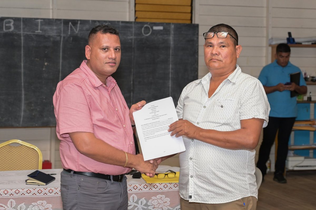 Minister of Housing and Water Collin Croal (left) handing over the contract to Toshao, Troy Peters.